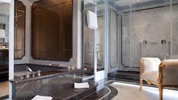 A luxurious bathroom with a large marble bathtub, a separate shower area, and a gold-framed armchair.