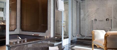 A luxurious bathroom with a large marble bathtub, a separate shower area, and a gold-framed armchair.