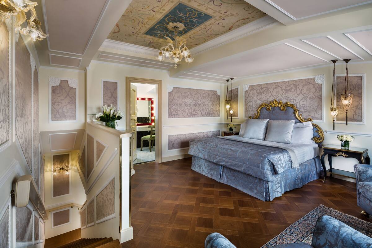 Une chambre spacieuse avec un grand lit, un plafond décoré et un escalier menant à une pièce adjacente.