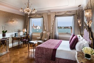 Una camera d'hotel con un letto, una scrivania, una sedia, una lampada e vista su un corpo d'acqua.