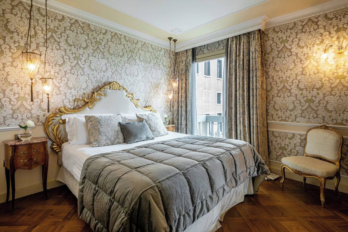 Une chambre à coucher avec un grand lit, une tête de lit décorée et un fauteuil classique.