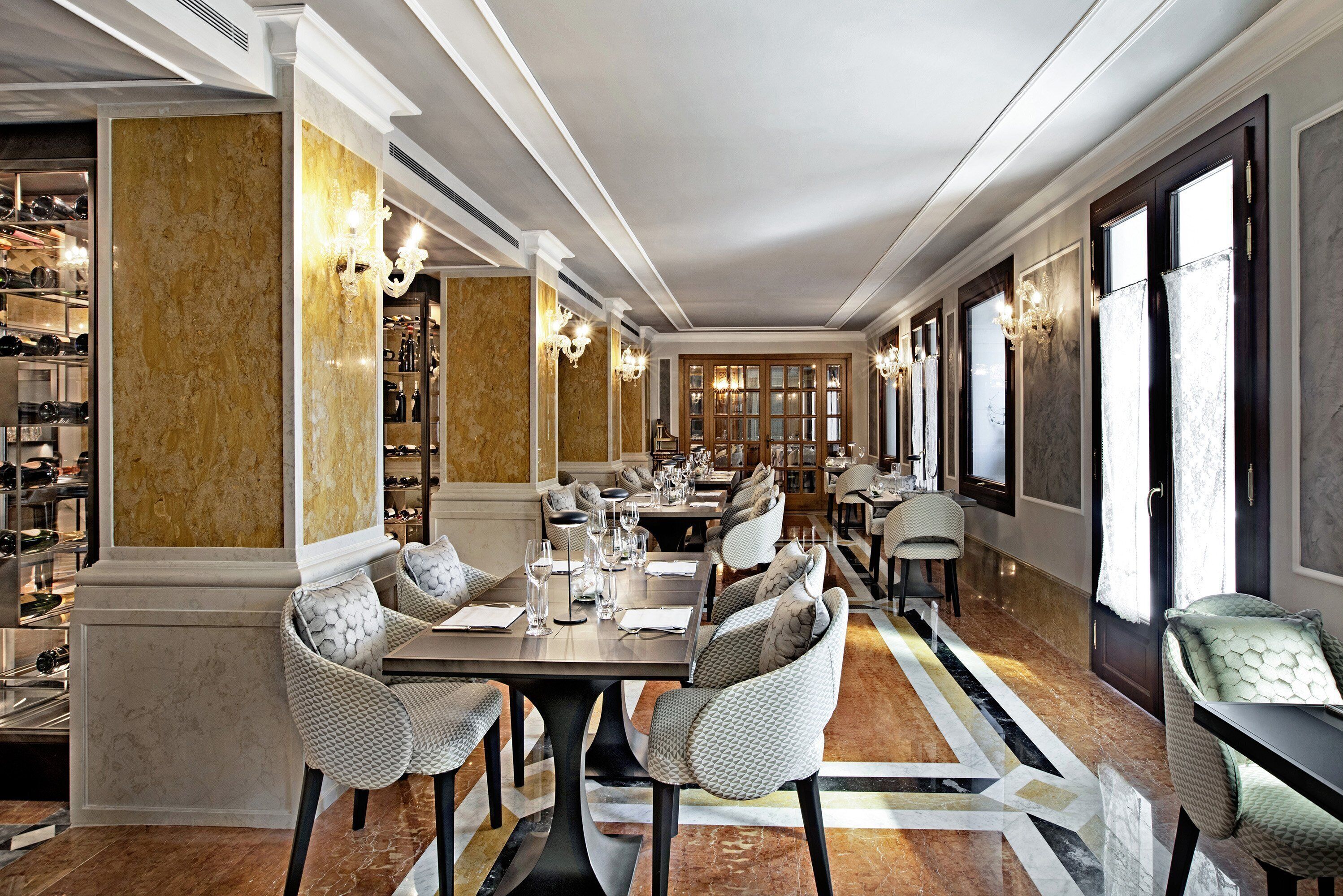 Une vaste salle à manger avec un sol en marbre, une longue table dressée pour un repas, et une cave à vin visible au fond.
