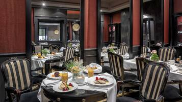 A dining area with multiple tables set for breakfast, featuring plates of food, drinks, and a vase of flowers.