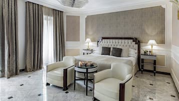 A hotel room with a large bed, two armchairs, a small round table, and two bedside tables with lamps.