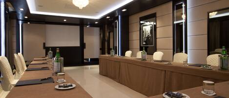 A conference room with a long table, chairs, a projector screen, and a large chandelier.