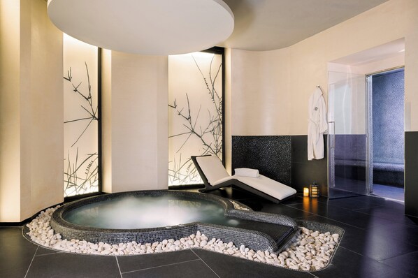 A spa room with a hot tub, a lounge chair, and a glass shower enclosure.