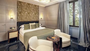 A modern bedroom with a large bed, two bedside tables, a nightstand, a round side table, two chairs, and a large window with curtains.