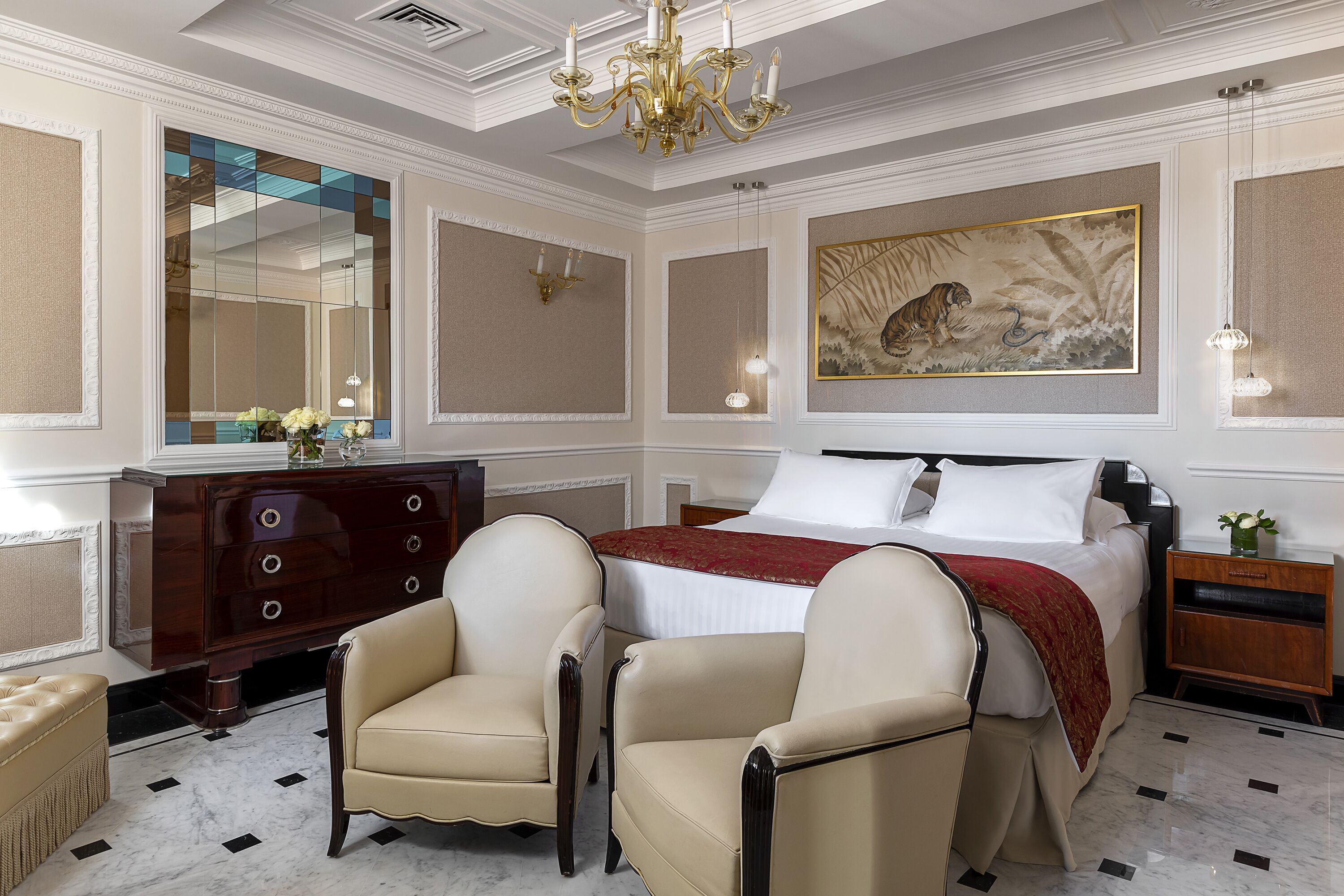 A bedroom with a large bed, two armchairs, a dresser, a mirror, and a painting on the wall.