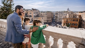 A family on a balcony overlooking a cityscape with historic buildings and a dome in the distance. - Baglioni Hotel Regina - The Leading Hotels of the World (Rome)