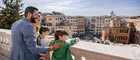 A family on a balcony overlooking a cityscape with historic buildings and a dome in the distance.