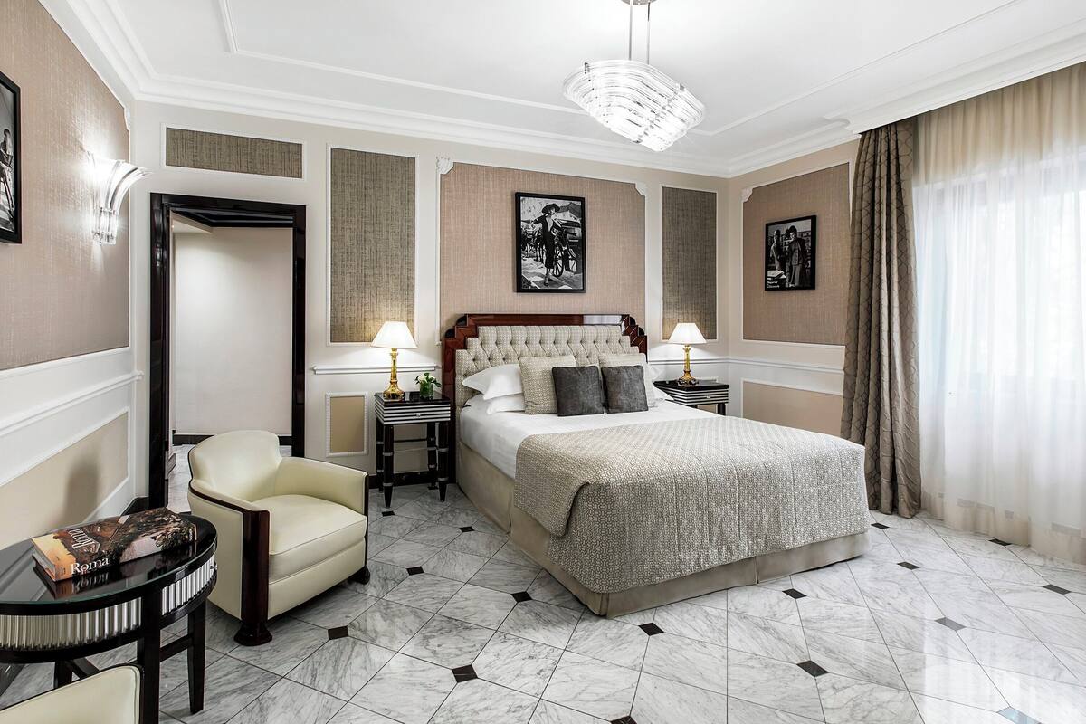 A hotel room with a large bed, a chair, a small table, and two nightstands with lamps.