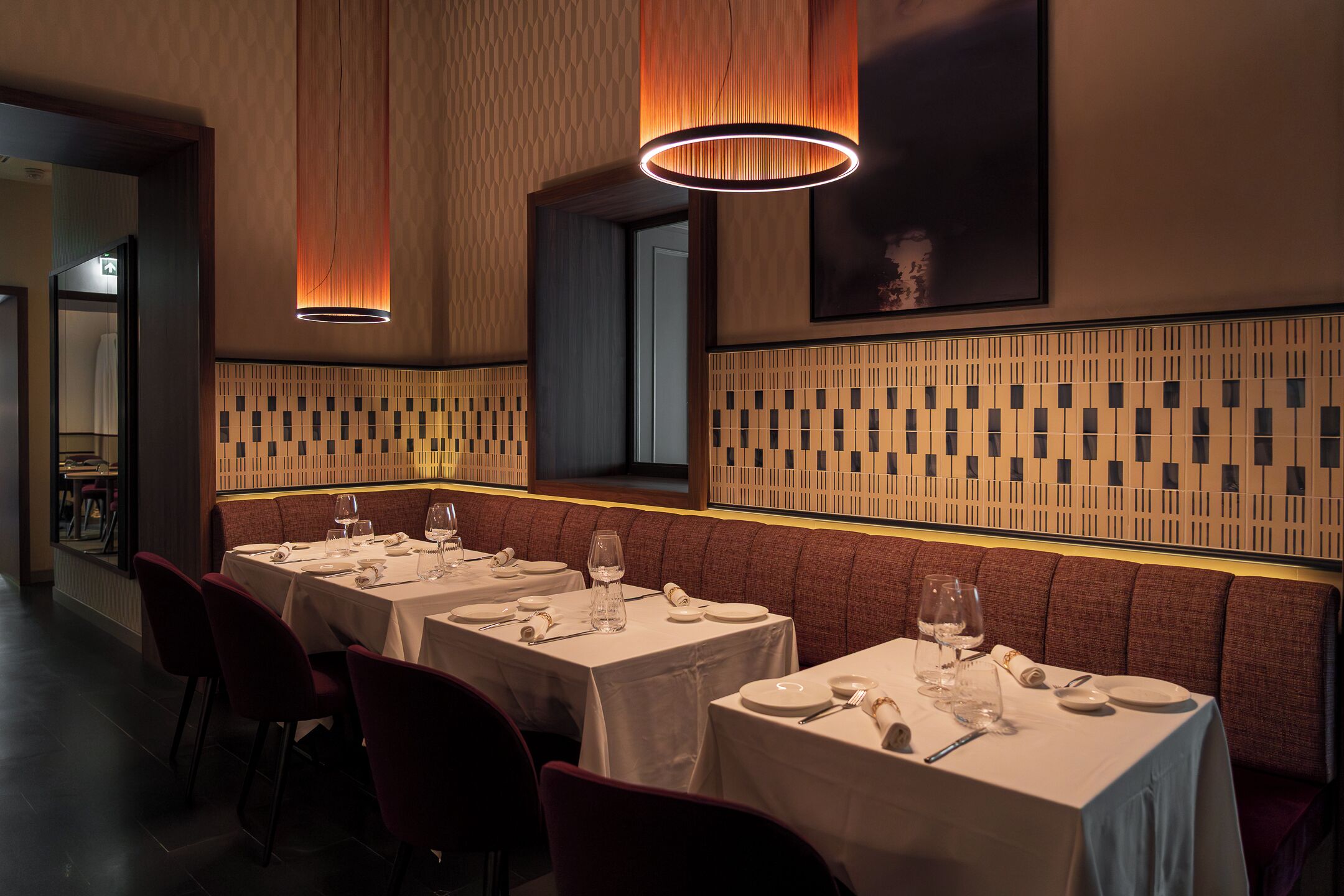 A restaurant interior with multiple tables, chairs, and a patterned wall design.