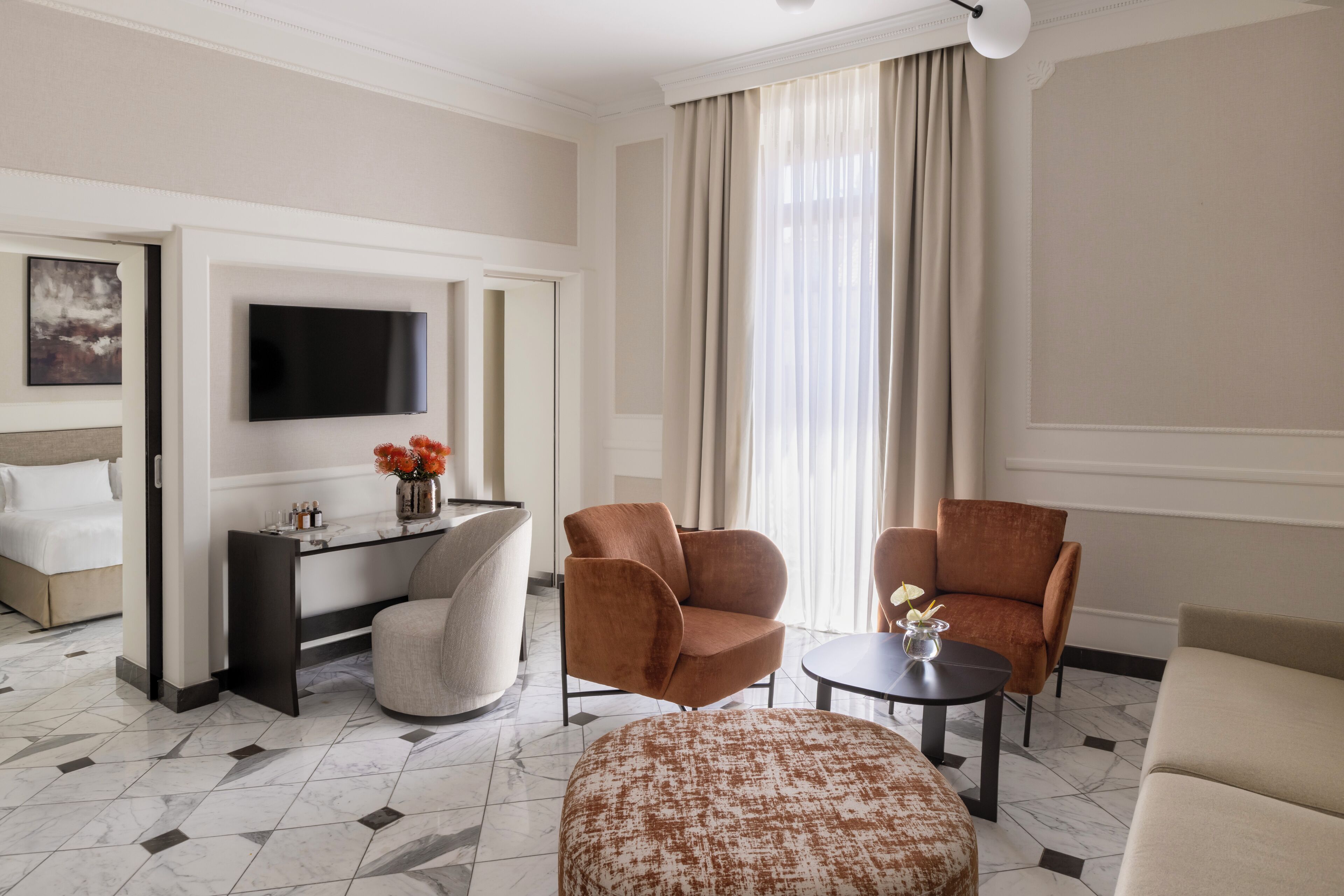 Hotelkamer met een bed, een bureau met een flatscreen-televisie, twee fauteuils, een bijzettafeltje en een groot raam met gordijnen.