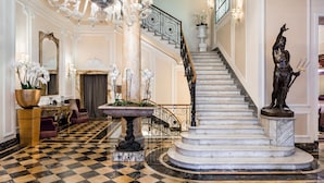 A grand lobby with a marble staircase, ornate chandeliers, and classical statues. - Baglioni Hotel Regina - The Leading Hotels of the World (Rome)