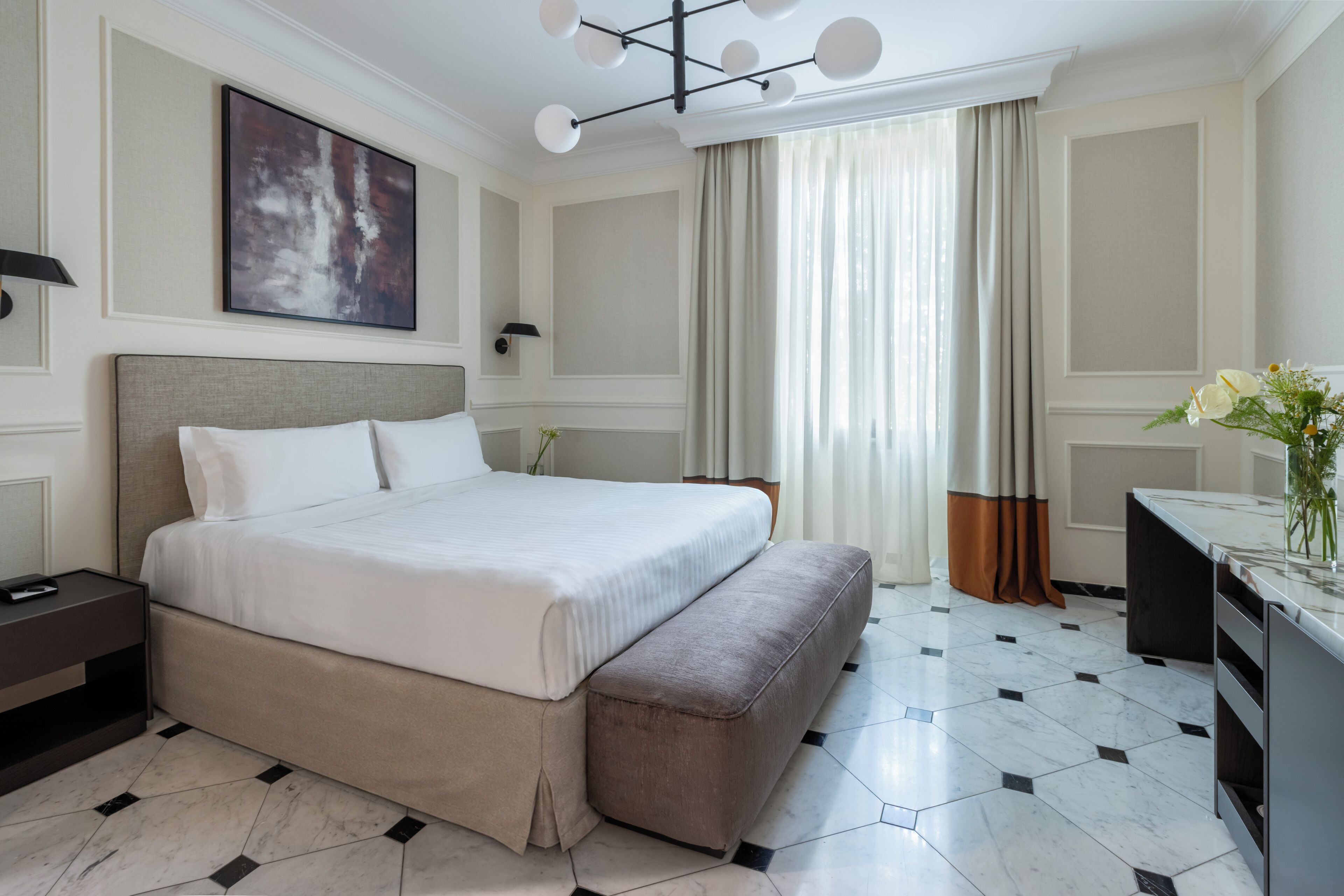 A hotel room with a large bed, a bedside table, a desk, and a chair.