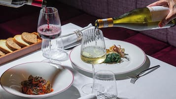 A table set with plates of food, glasses of wine, and a bottle being poured.