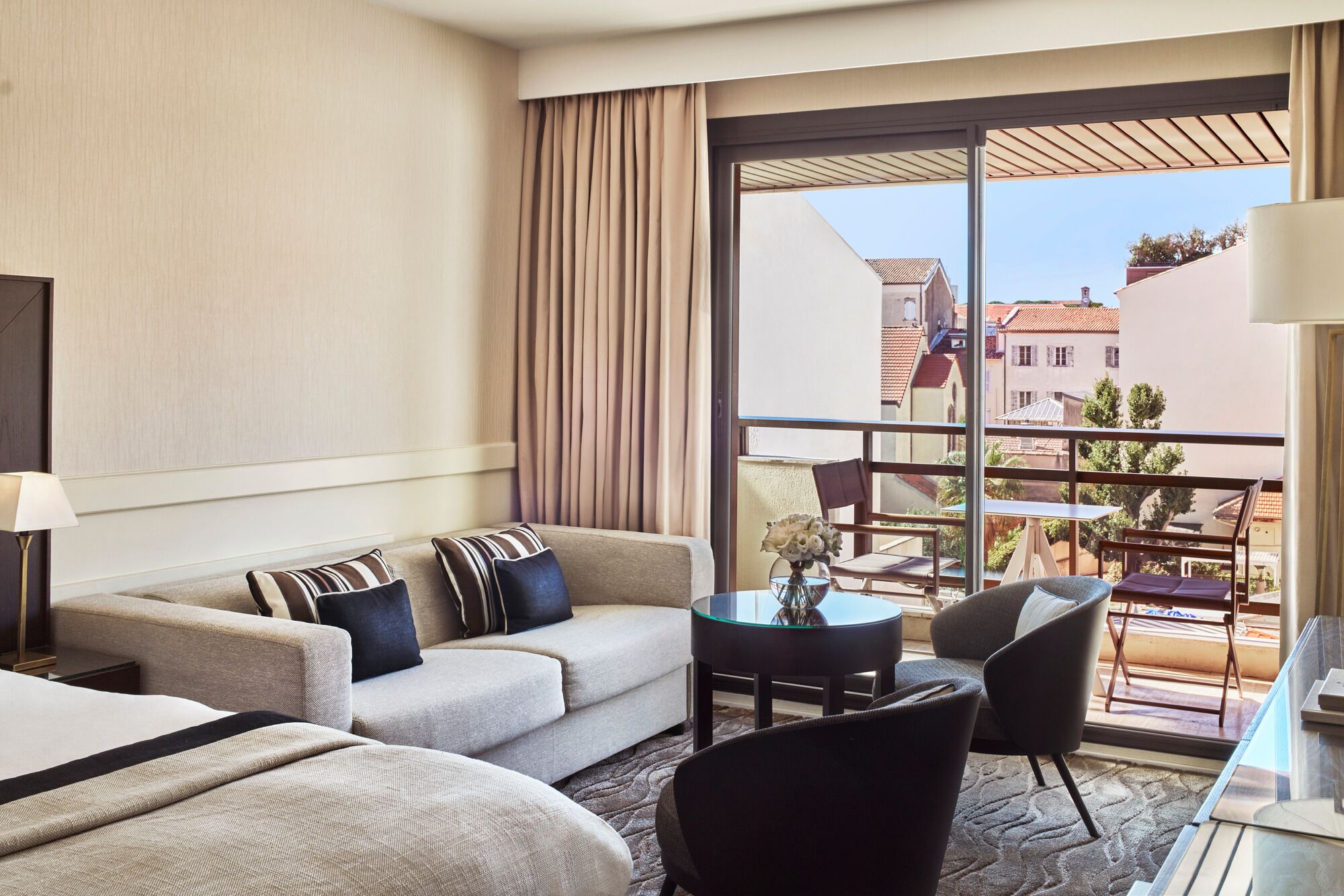 A hotel room with a sofa, two armchairs, a small table, and a balcony with a view of buildings.