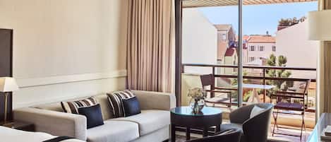 A hotel room with a sofa, two armchairs, a small table, and a balcony with a view of buildings.