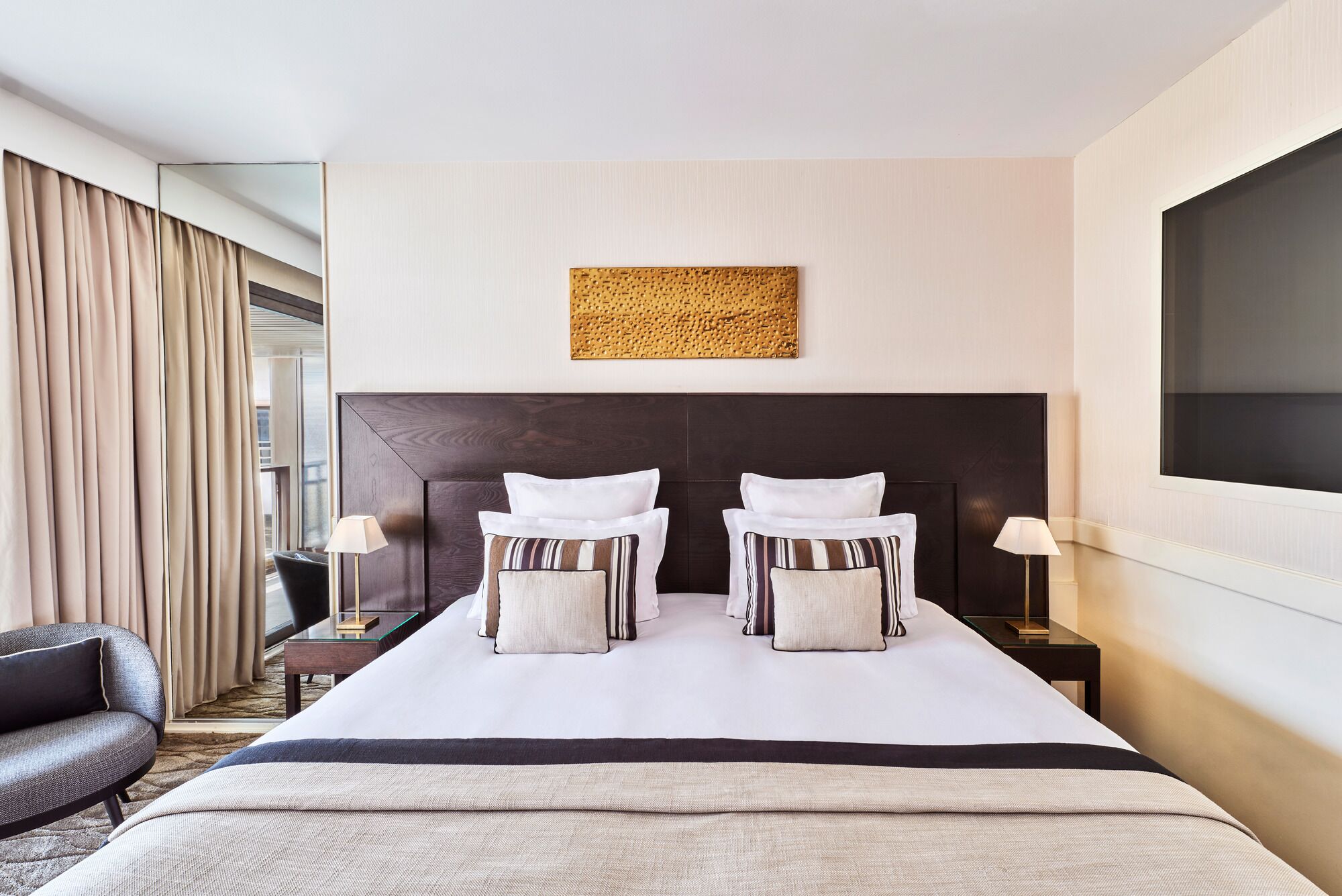 A hotel room with a large bed, two bedside tables, a chair, and a large window.
