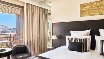 A hotel room with a large bed, a view of the city, a chair, and a table.