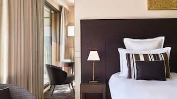 A hotel room with a large bed, a bedside table with a lamp, a chair, and a view of the outdoors through the window.