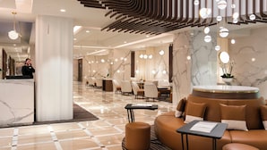 A modern hotel lobby with marble flooring, a reception desk, seating areas, and contemporary lighting fixtures. - Hôtel Barrière Le Gray d'Albion (Cannes)