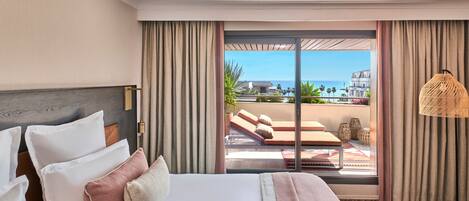 A hotel room with a bed, a view of the ocean, and a balcony with outdoor furniture.