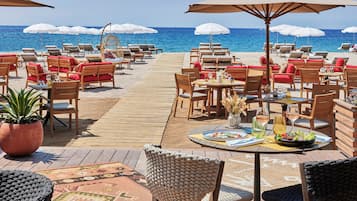 Een restaurant aan het strand met terras, inclusief tafels, stoelen en parasols voor beschutting.