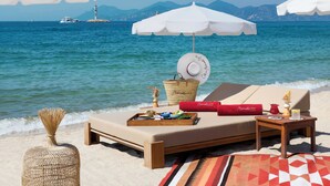 A beachside lounge with a view of the sea, a boat, and a lighthouse in the background. - Hôtel Barrière Le Gray d'Albion (Cannes)
