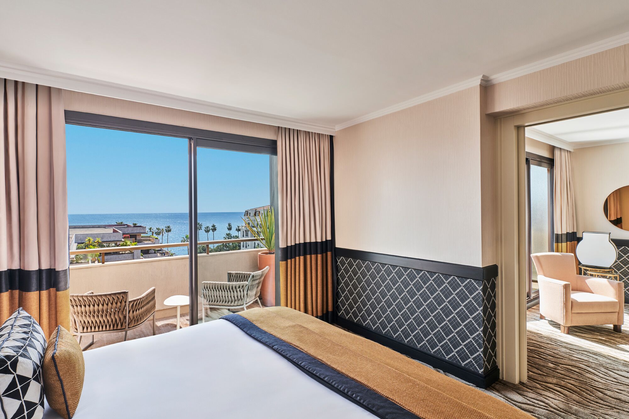 A hotel room with a large bed, a balcony with a view of the sea, and a sitting area with a chair and table.