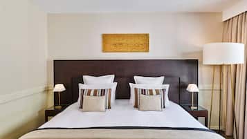 A hotel room with a large bed, two bedside tables, a headboard, a wall-mounted artwork, and a window with curtains.
