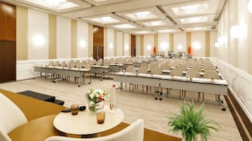 Une salle de conférence avec des rangées de tables et de chaises, un pupitre et une grande fenêtre.