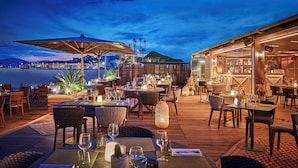 An outdoor dining area with tables set for dinner, overlooking a body of water at dusk. - Hôtel Barrière Le Gray d'Albion (Cannes)
