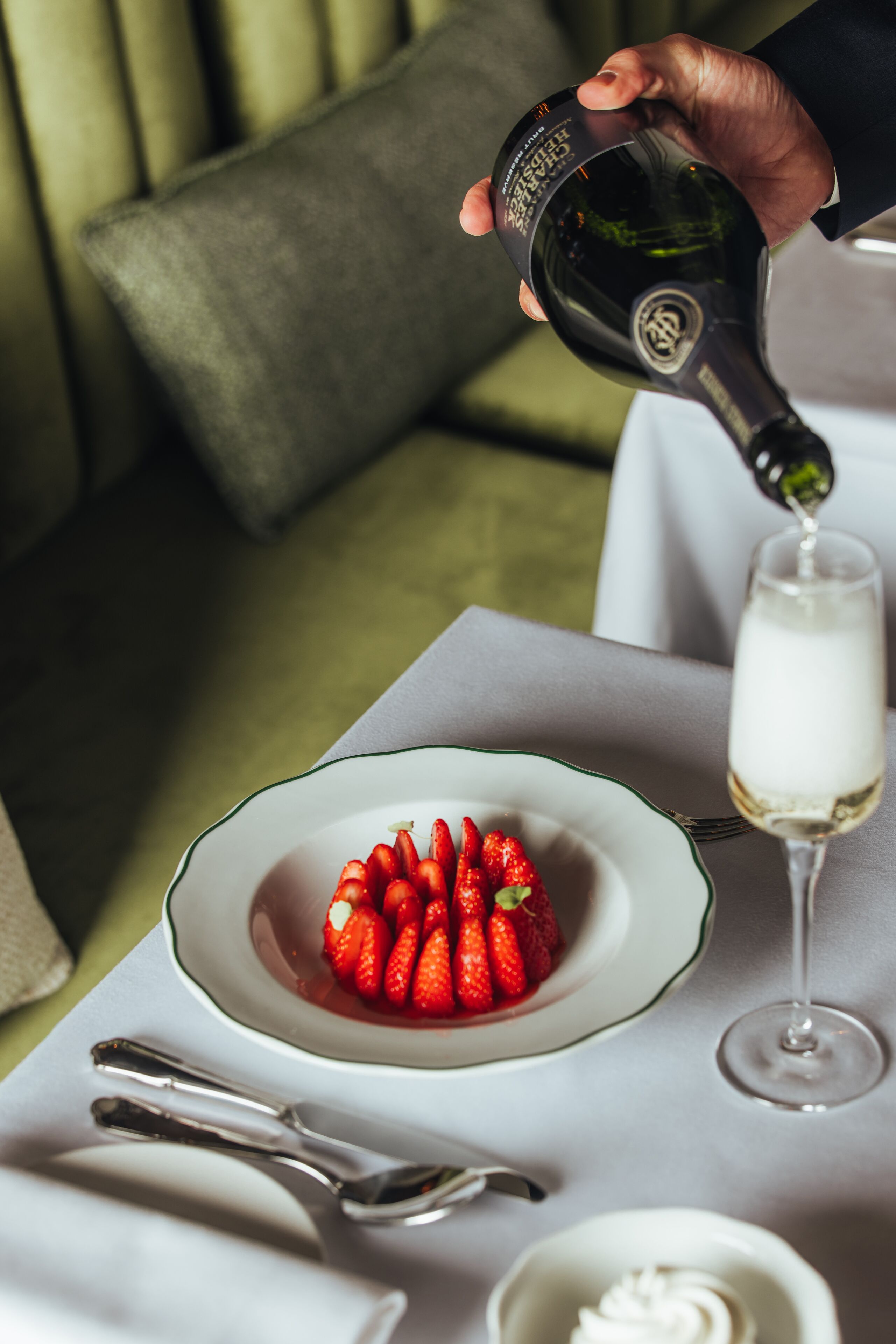 Una mano sirve una bebida en un vaso junto a un plato de fresas.