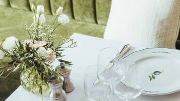 A table set for dining with white plates, silverware, and clear glasses, accompanied by a floral centerpiece and salt and pepper shakers.