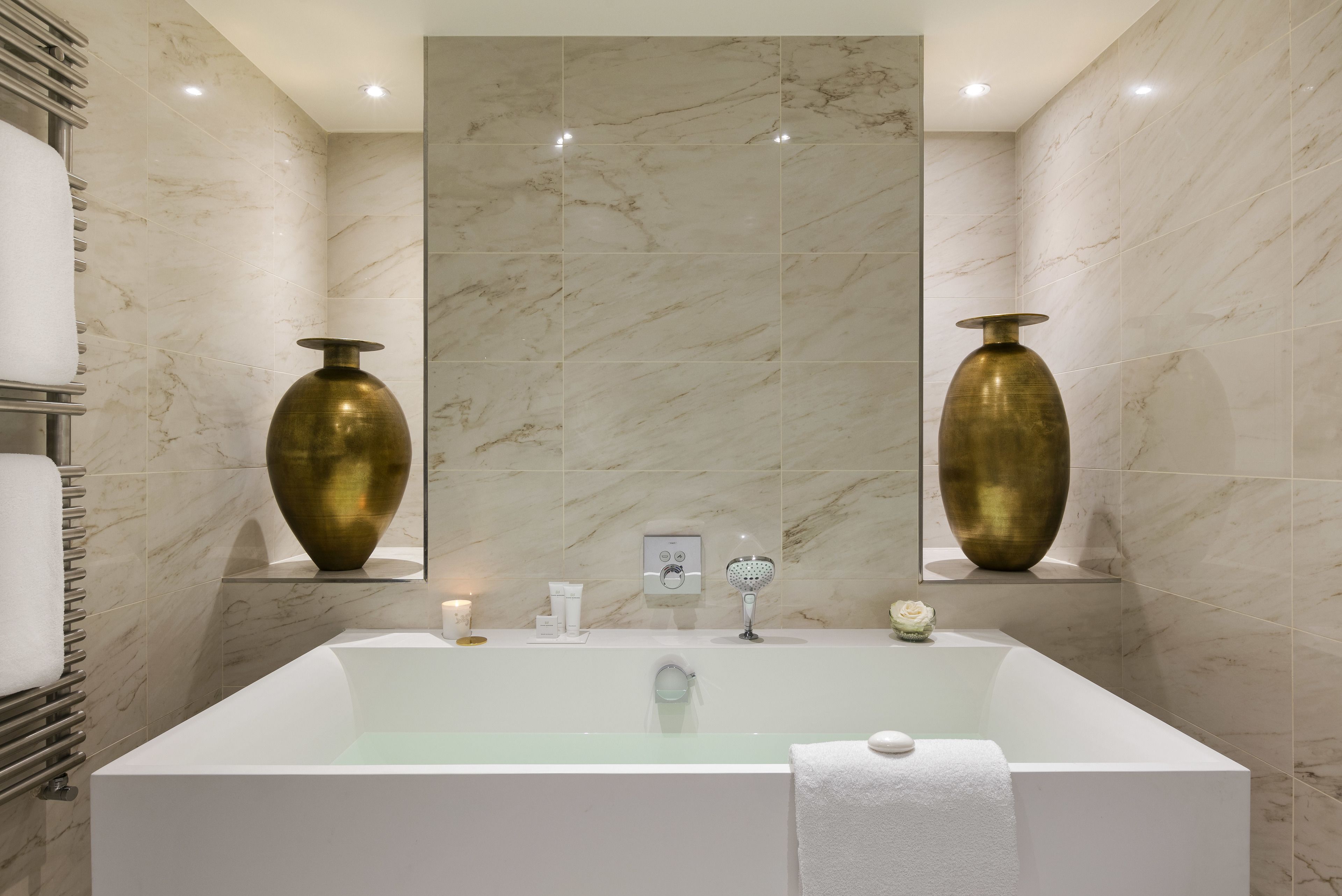 Ein modernes Badezimmer mit einer großen Badewanne, Marmorwänden und zwei großen Messingvasen an der Wand.