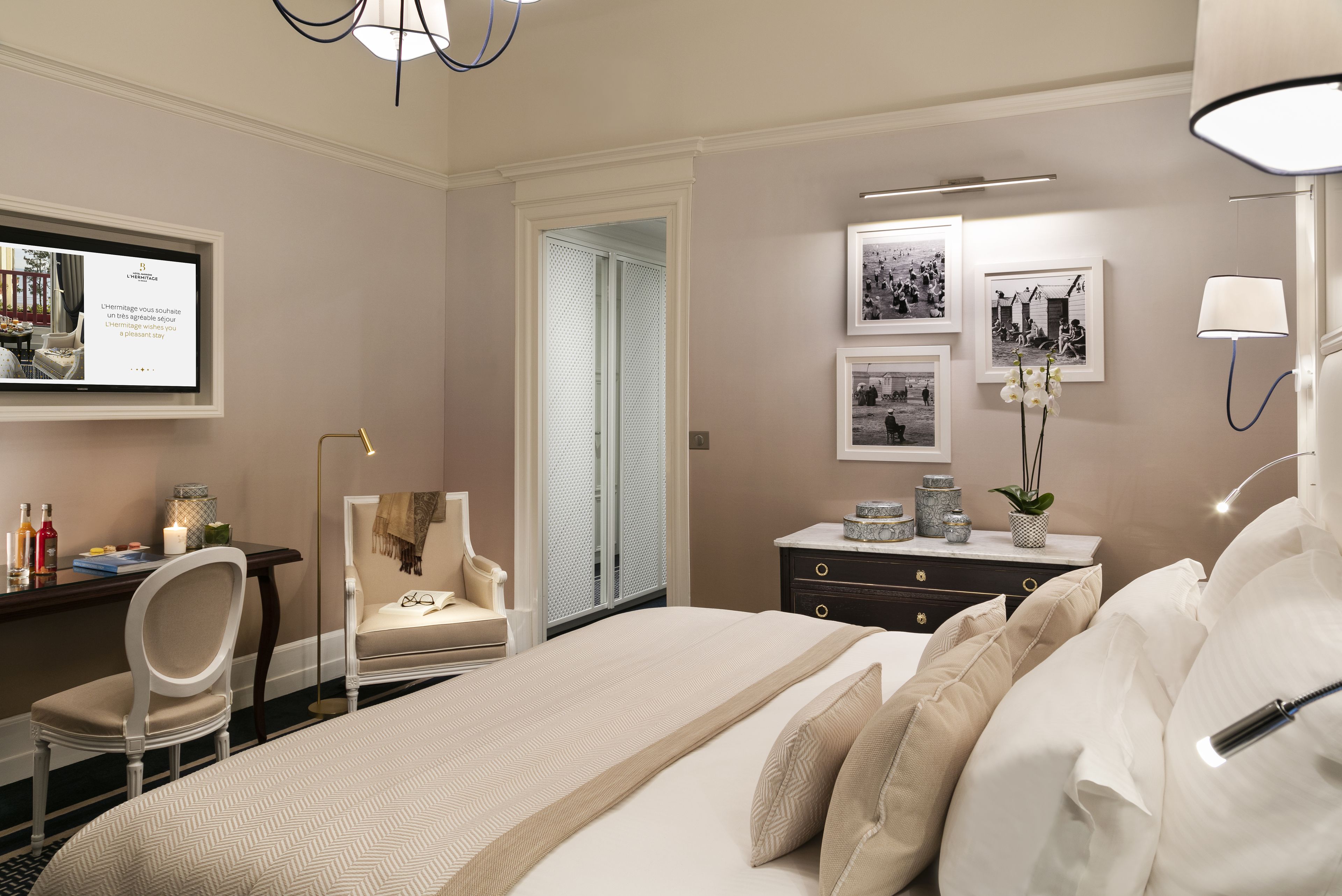 Habitación de hotel con una cama grande, un escritorio con silla, un aparador y fotografías enmarcadas en la pared.