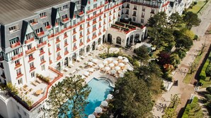 Un hotel gran amb diverses plantes, piscina exterior i gandules.