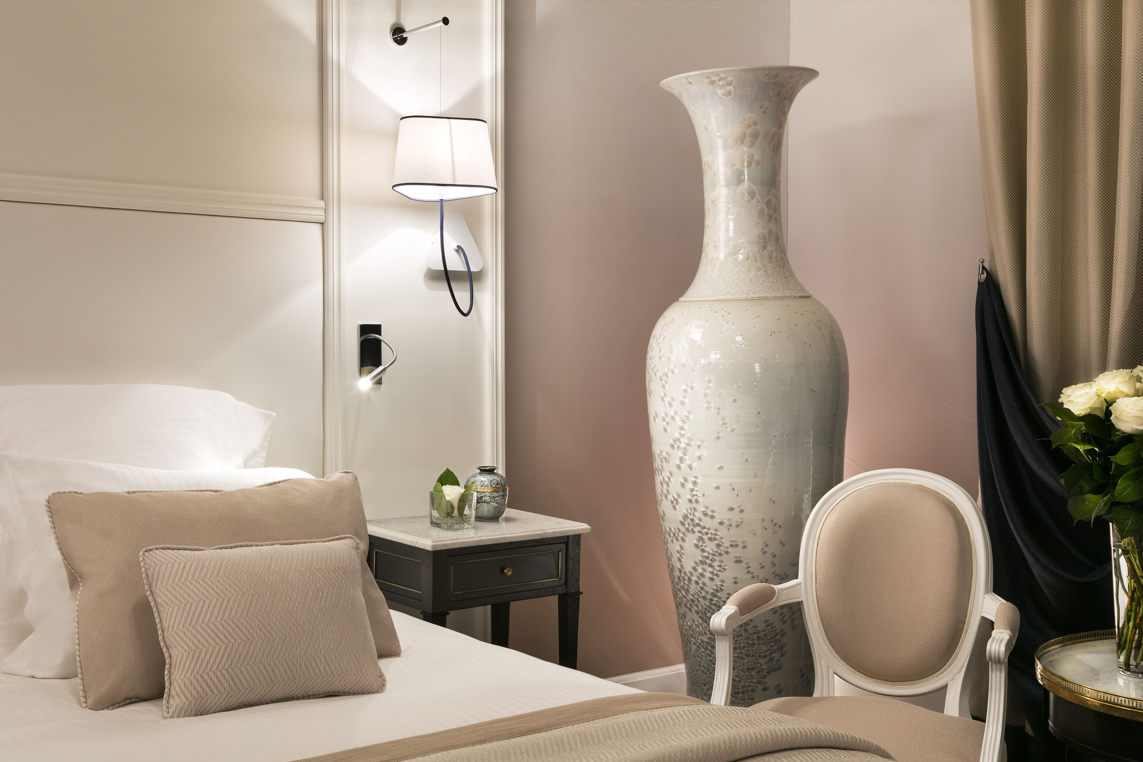 Une chambre d’hôtel avec un lit, une table de chevet, un grand vase et une chaise.