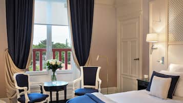 A hotel room with a bed, two chairs, a small table, and a vase of flowers.