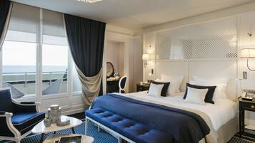 Une chambre d’hôtel avec un grand lit, un bureau, une chaise, une petite table et une vue sur la mer.