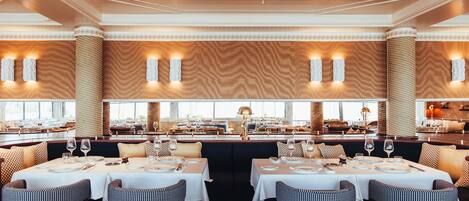 Een restaurant met een centraal zitgedeelte, tafels met witte tafelkleden en uitzicht op de eetruimte door grote ramen.