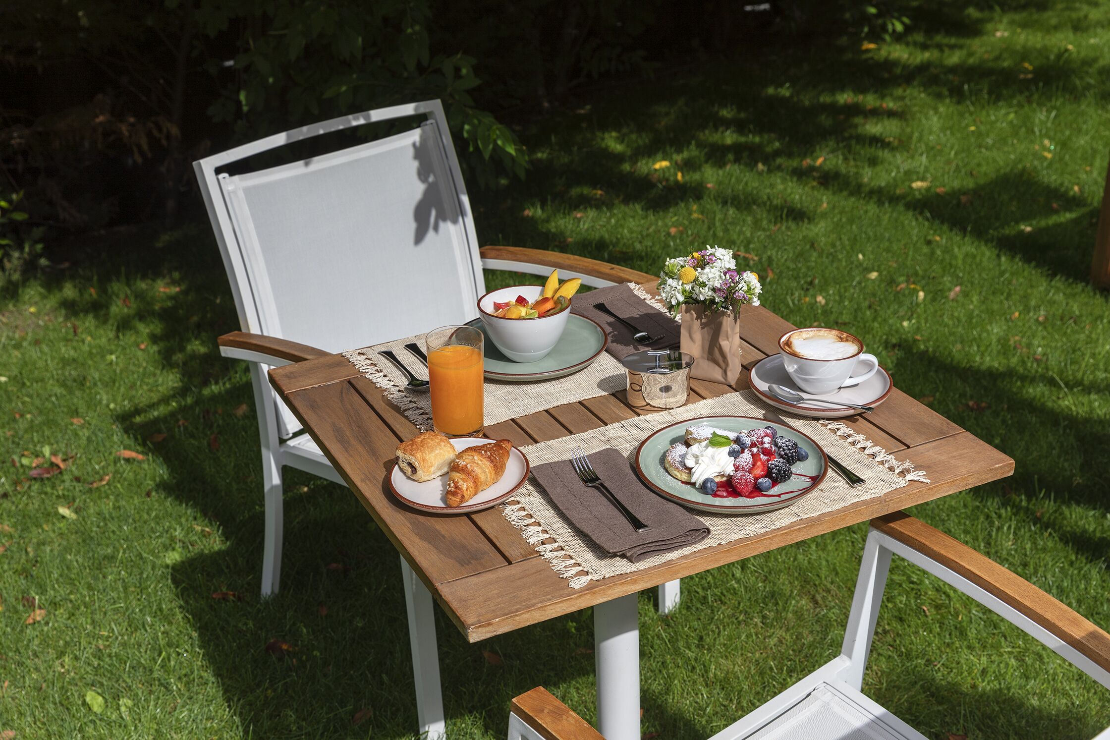 A wooden table set with breakfast items including croissants, a bowl of fruit, a glass of orange juice, and a cup of coffee.