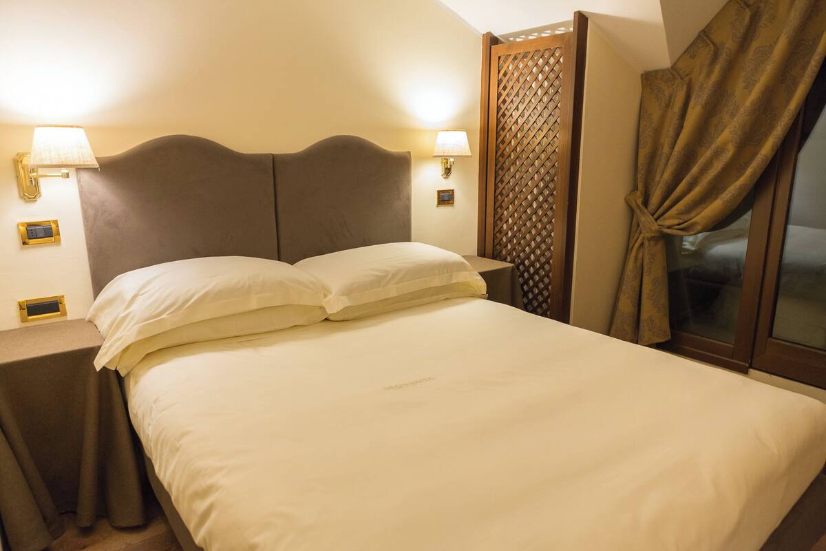 A neatly made bed with white linens, two bedside lamps, and a wooden headboard.