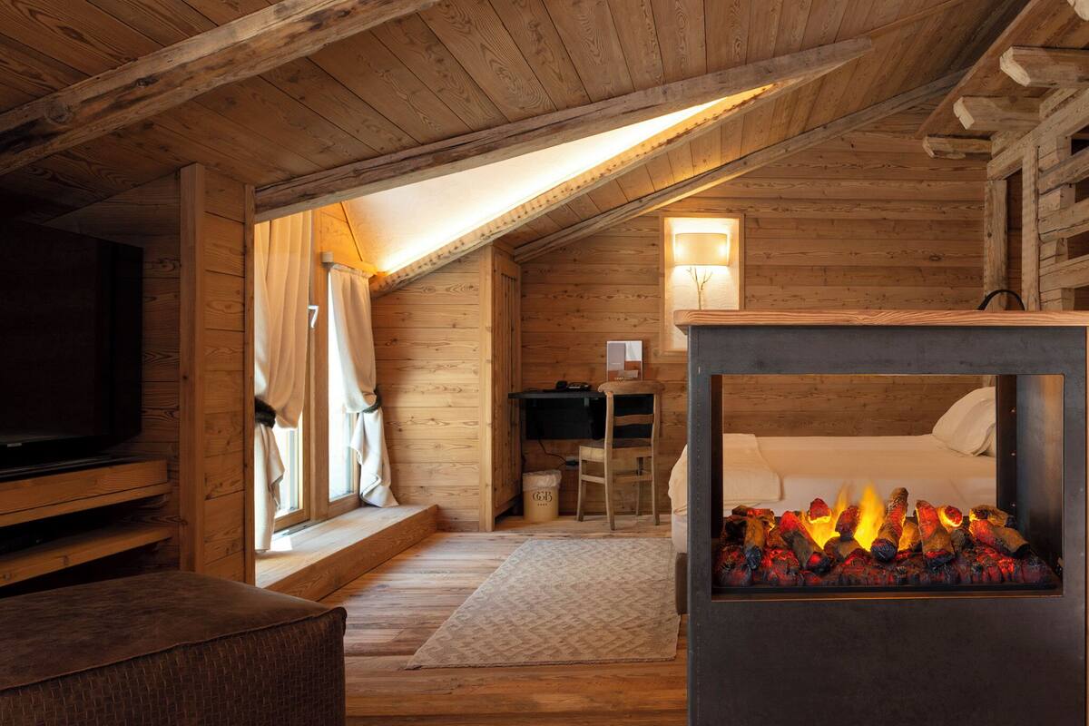 A cozy log cabin room with a fireplace, a bed, a desk, and a television.