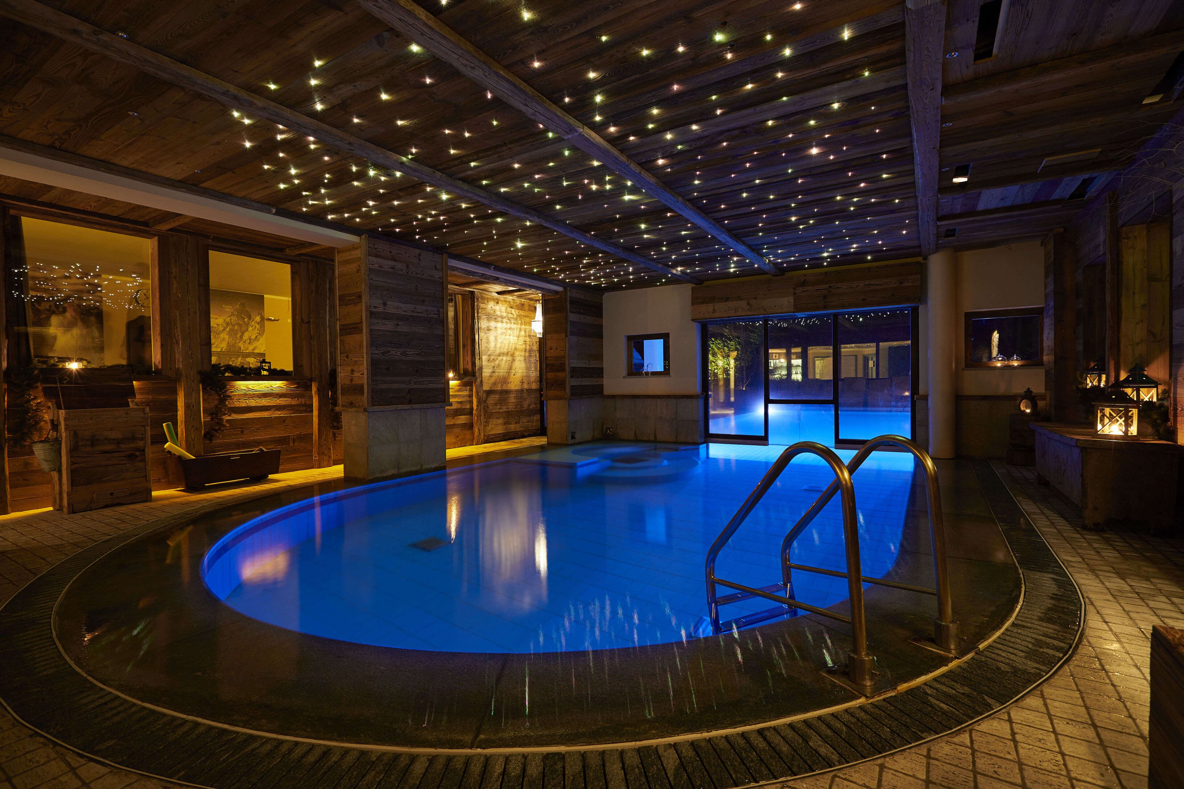 A swimming pool with a blue hue, surrounded by wooden walls and a tiled floor.