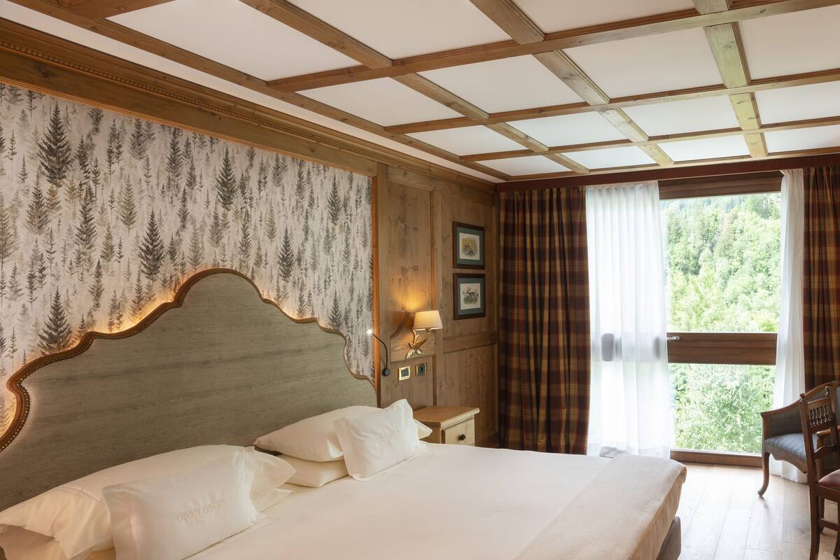 A hotel room with a large bed, a desk with a chair, a television, and a window with curtains.