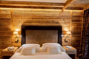 A wooden-paneled room with a large bed, two bedside lamps, and a nightstand with a book and a phone. - Gran Baita Hotel & Wellness (Courmayeur)