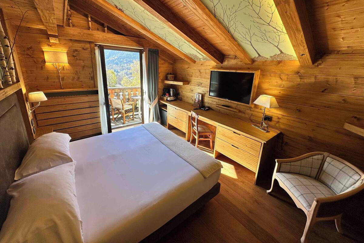 A wooden cabin room with a bed, desk, chair, and a TV.