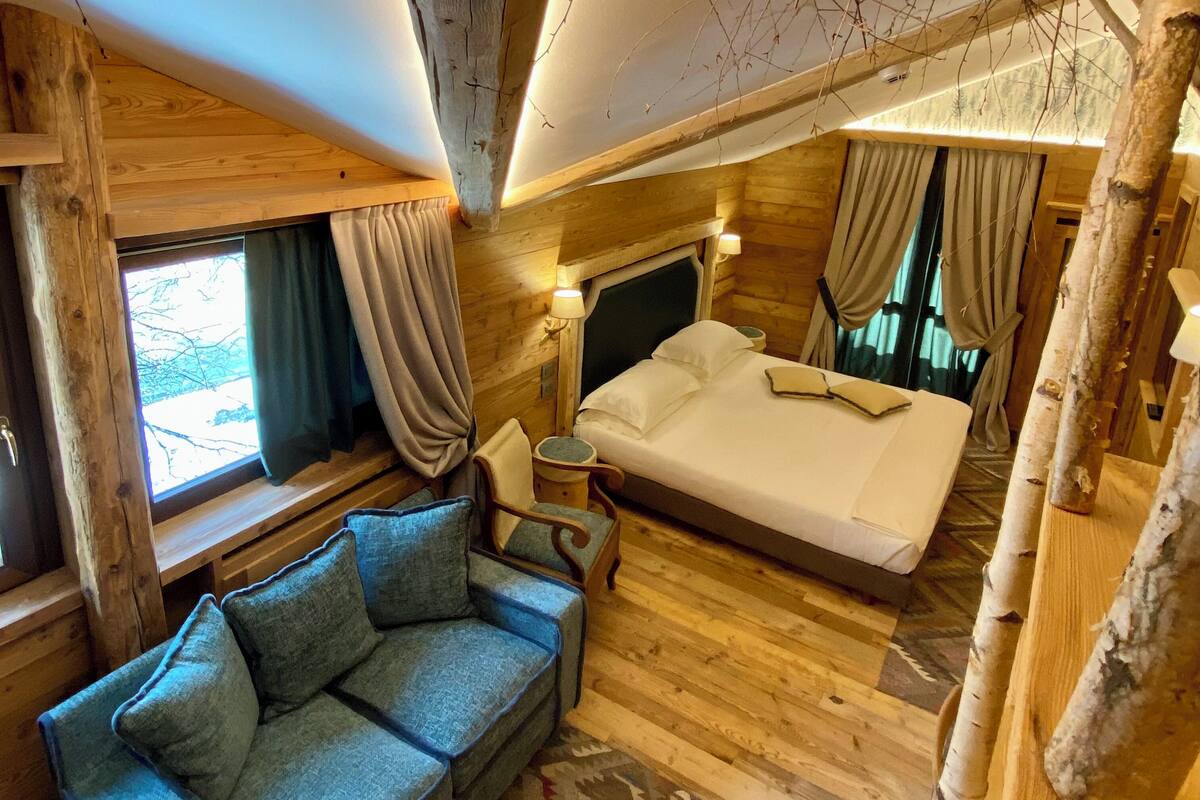 A cozy cabin-style room with a bed, a sofa, and a window with curtains.